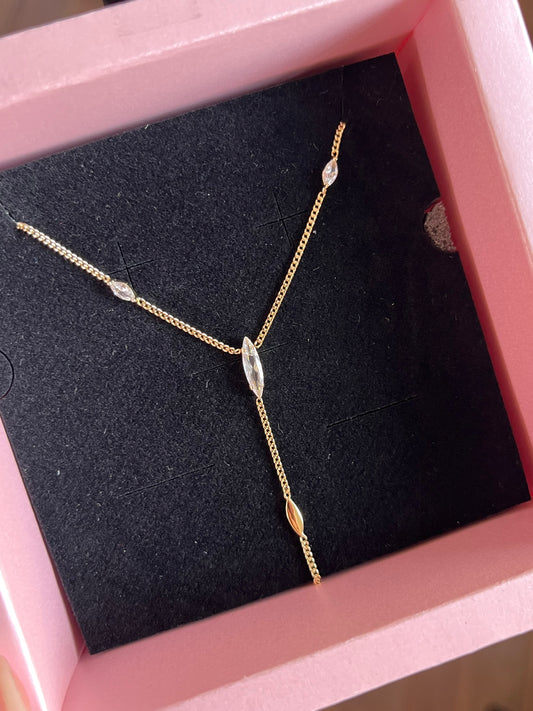 A delicate gold Y-shaped necklace with marquise-cut clear stones, displayed inside a pink jewelry box with a black velvet insert.