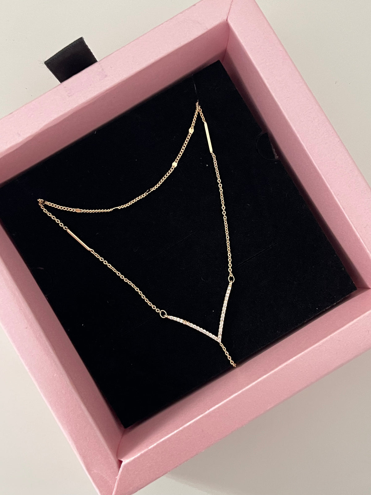 A delicate gold chain necklace displayed on a black velvet insert inside a pink jewelry box.