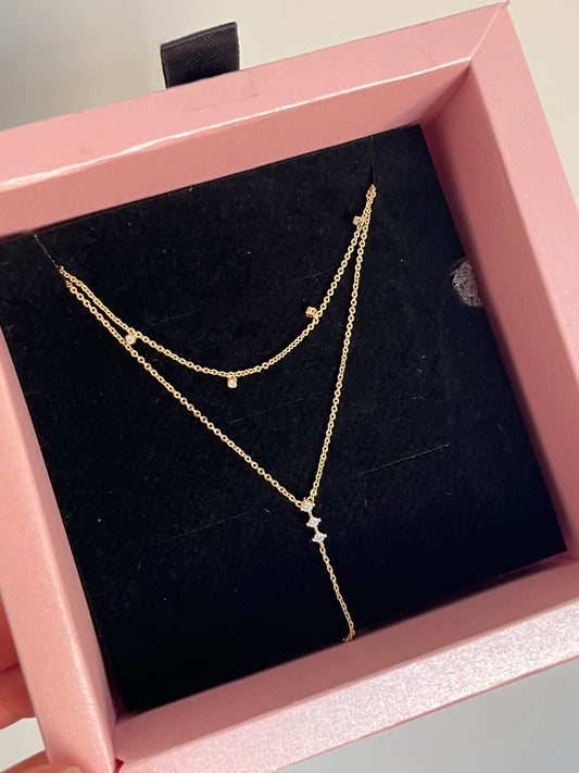 A delicate gold chain necklace with small star and dot charms, displayed inside a pink jewelry box with a black velvet lining.